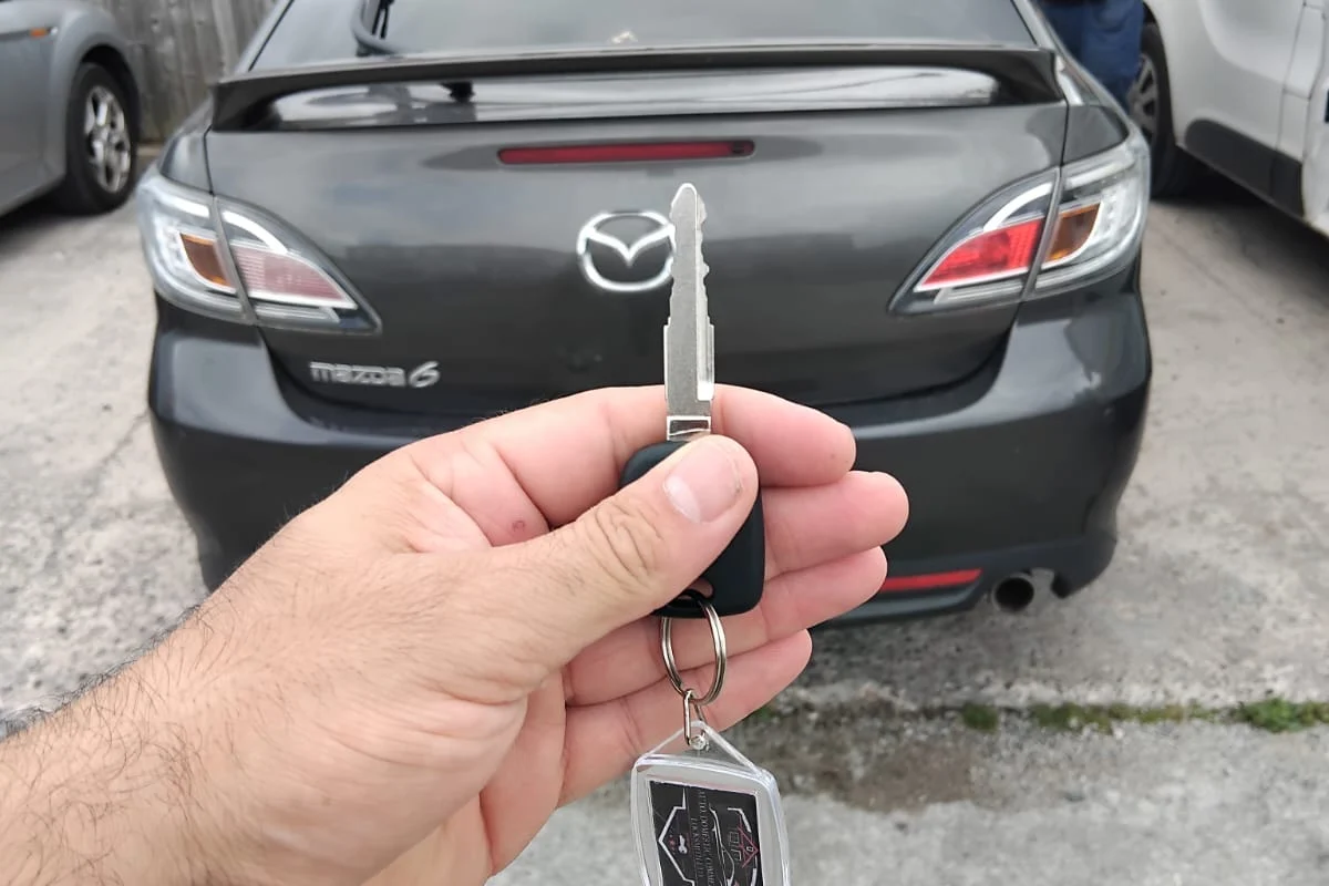 Replacement Mazda key held beside the car