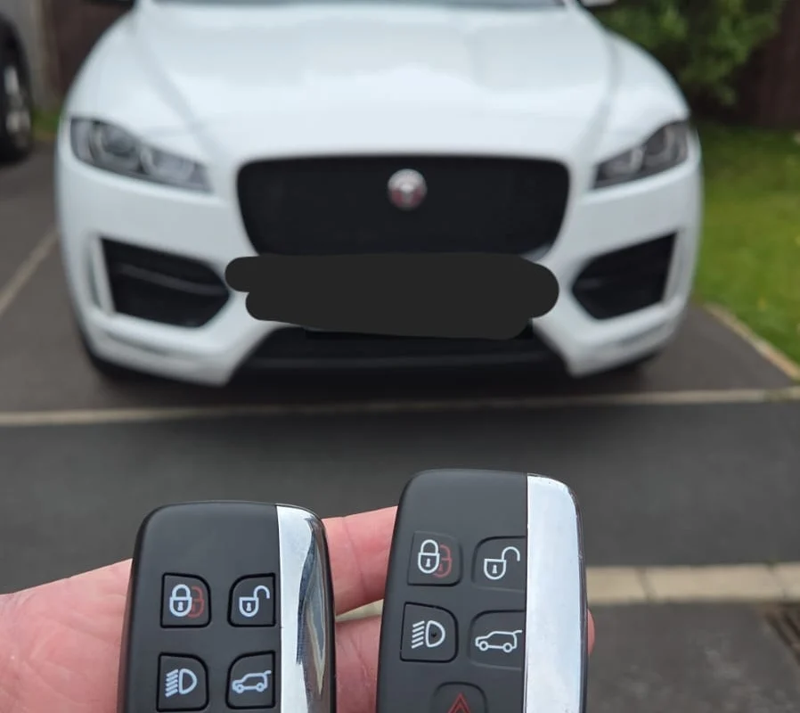 Jaguar smart keys beside a white Jaguar saloon