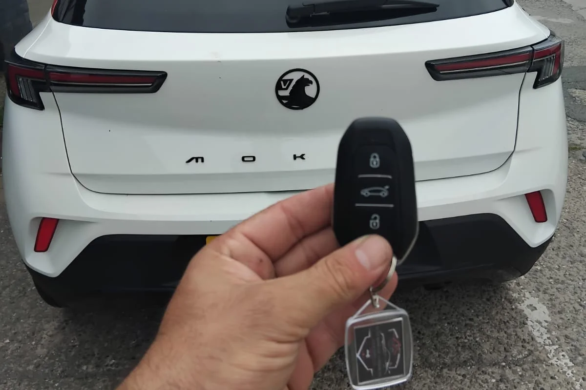 Vauxhall flip key with three buttons held behind a white Vauxhall Mokka